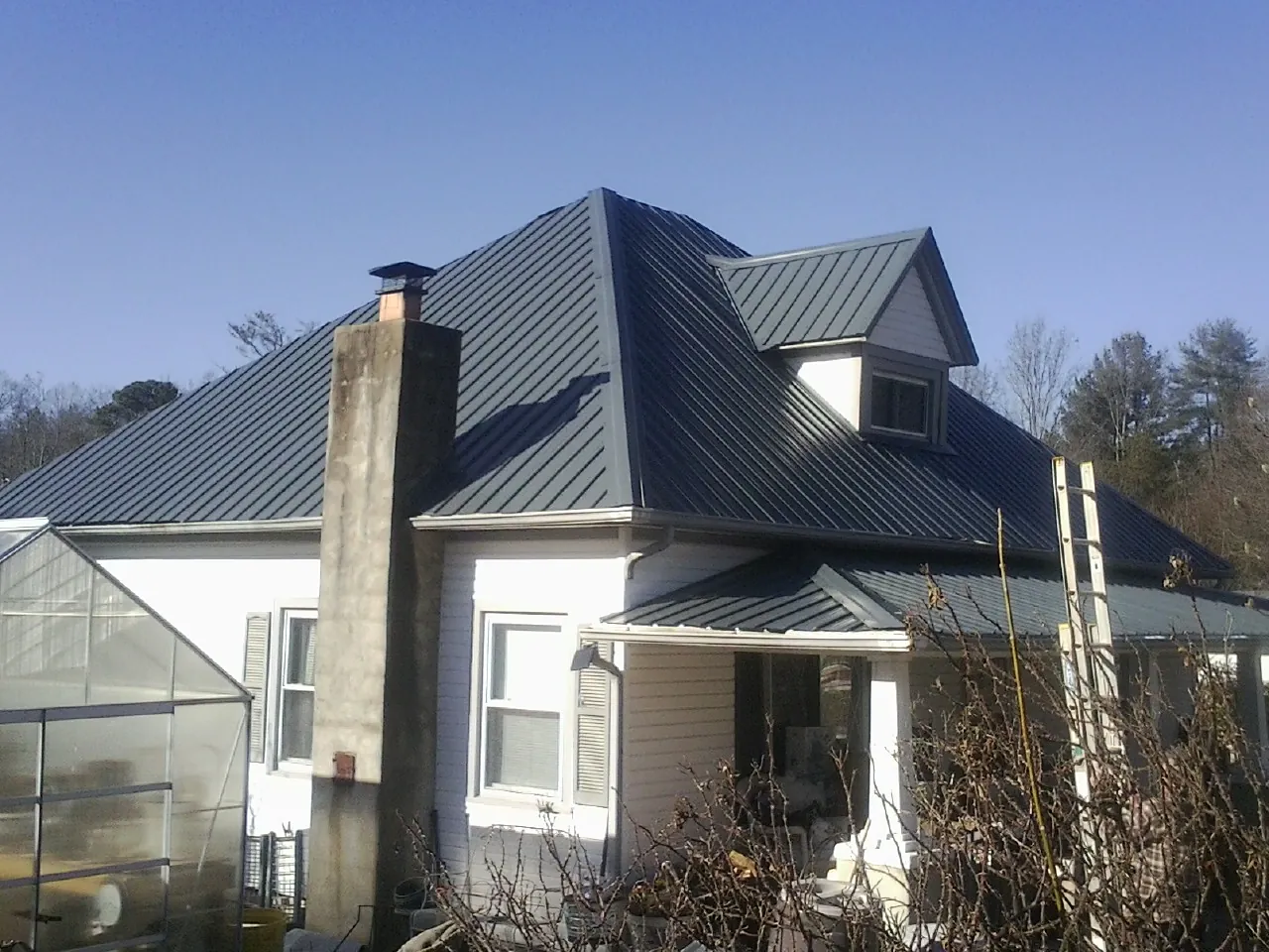 Dark blue standing seam metal roof on a white farmhouse with dormer — Slate & Tile Roof Repair by Roofing Brothers in Mchenry