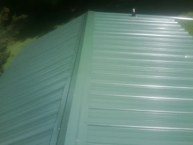 New green metal panels meeting at the ridge of a roof — Flat Roof Repair work by our crew in Mchenry