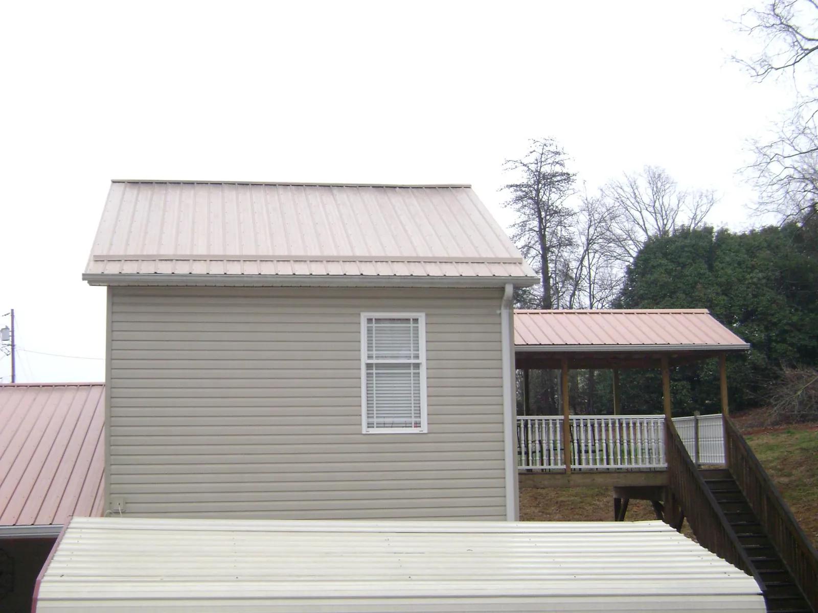 Tan metal roofs on a two story addition and attached porch, from a Roof Replacement job in Mchenry